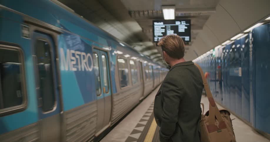 White man talking on his cellphone while waiting for the train to arrive at the metro