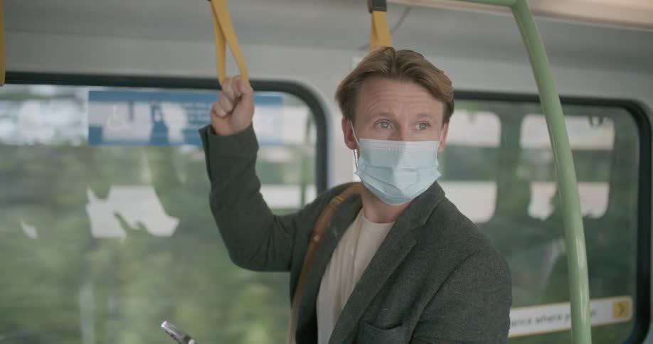 A man standing tapping on a smart phone while holding on to a grip on a moving train at daytime