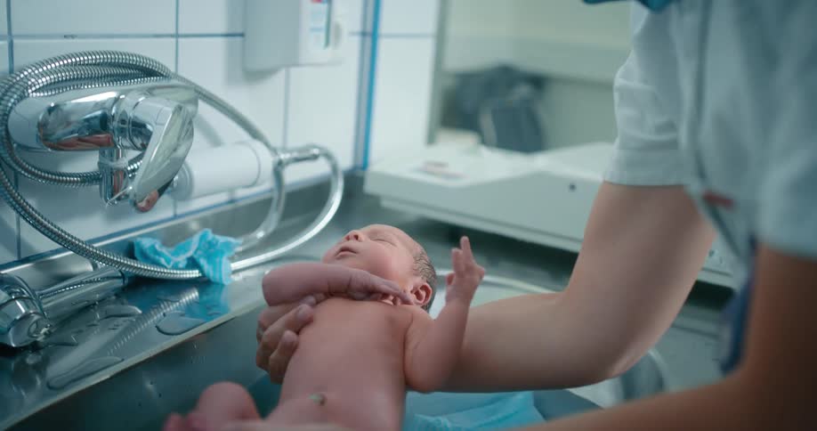 A nurse rushes to place a newborn in a sink filled with water