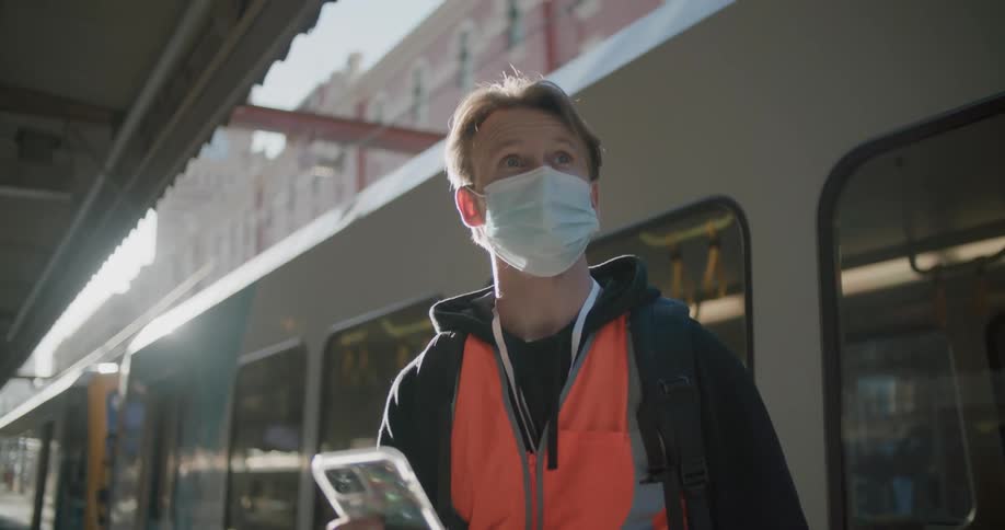 White working man wearing a mask and using his cellphone in a train station