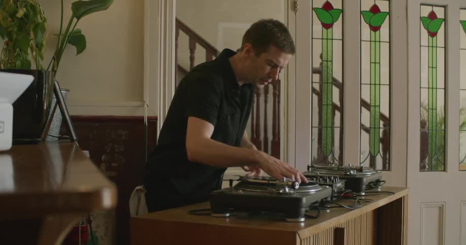 A man sets up an area with a record player and mixing equipment indoors