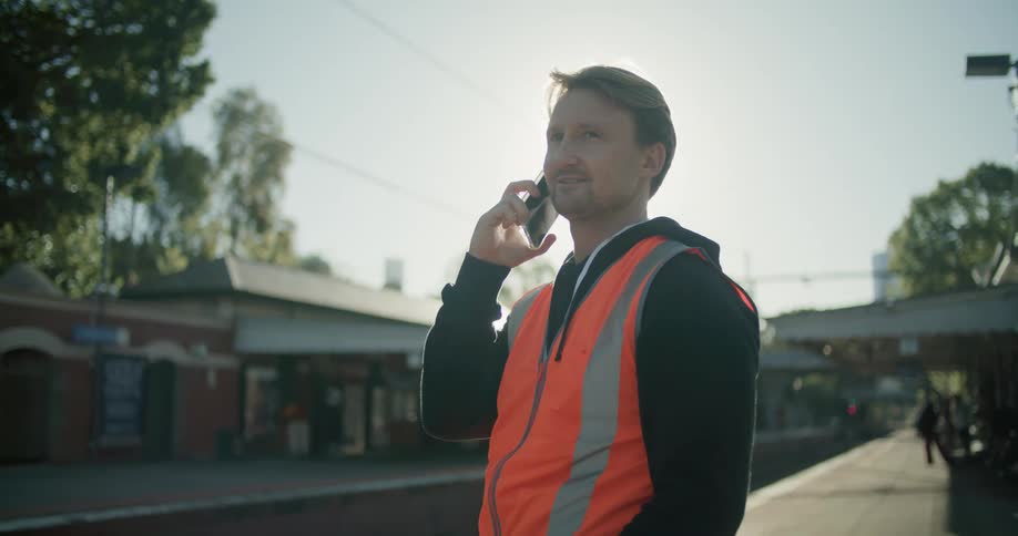 Man wearing a bright red vest talking on a cellphone in a train station at evening