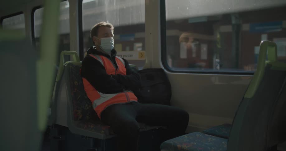 A man wearing a mask sits asleep on a bus as it drives along
