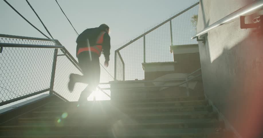 A person with a backpack and a mask walking up a stairs with the sun the sky and clouds in the background