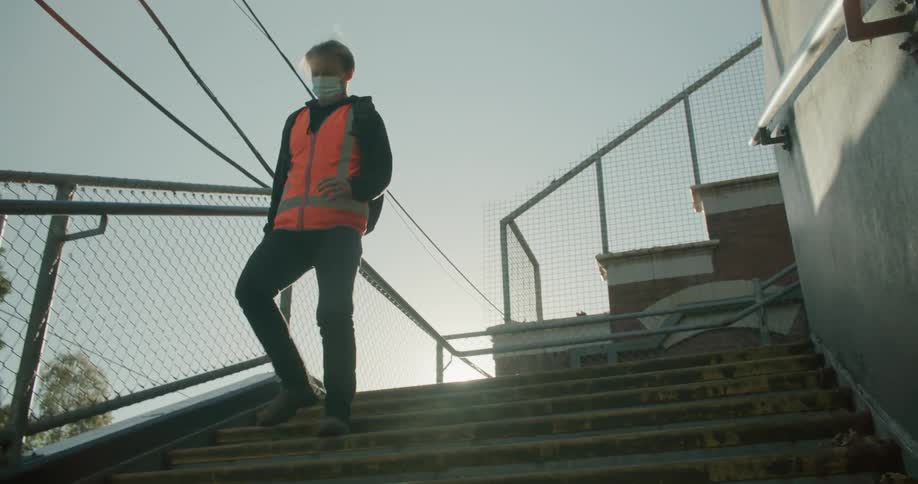A man walks down a flight of exterior stairs wearing an orange vest and a face mask