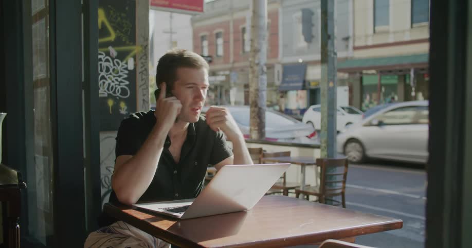 A man using a laptop while talking on the phone