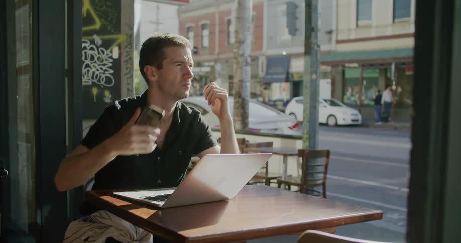 Man talking on his cellphone and then typing on his laptop in a bar