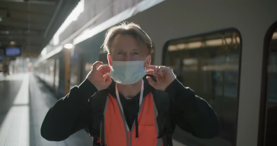 White working man putting a mask on in front of a train