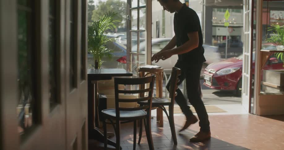 A man in a restaurant taking chairs from a table and placing them on the floor