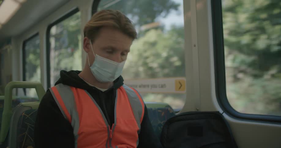 A blonde man sits on a train looking at his cell phone
