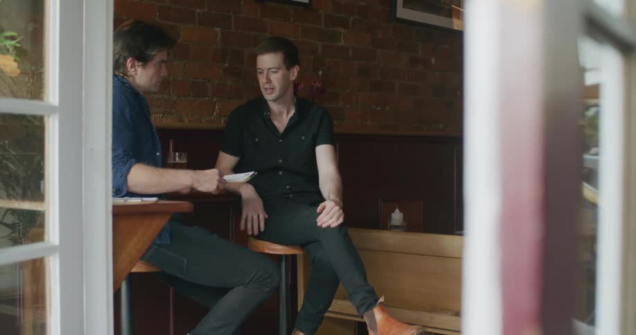 Two white men talking to each other sitting at a table in a bar
