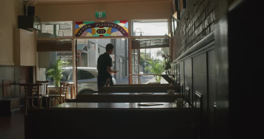A man placing menus onto tables inside of a restaurant at daytime