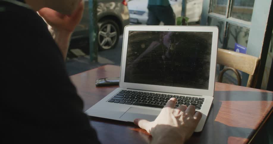 Young man sitting in an outdoors cafe in front of a laptop over the table