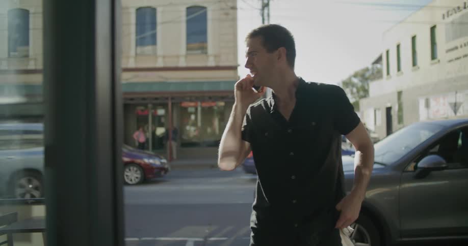 A man talking on a phone in a city while waving to someone