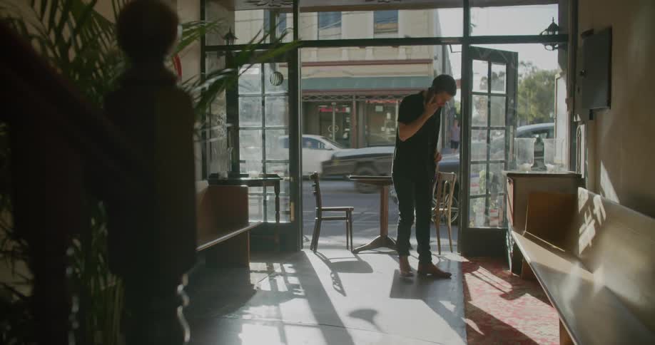 A man speaks on his smartphone as he paces back and forth in the entryway of a building in a city during the day