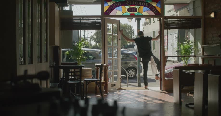 An employee unlocks and opens up the doors to a restaurant as people walk past