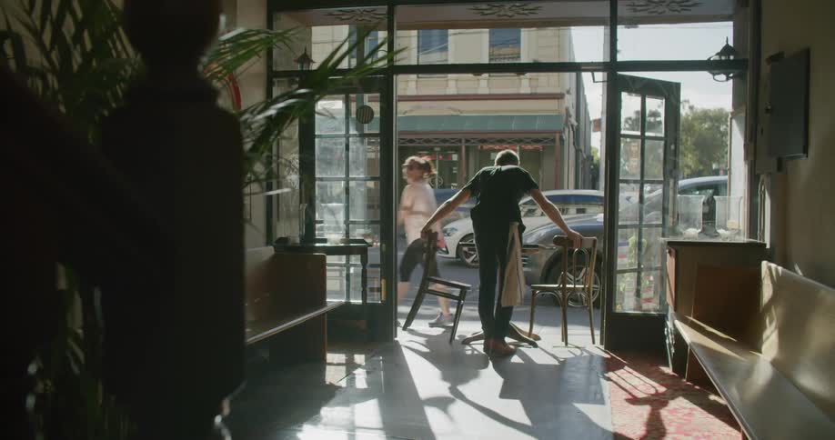 An employee in a restaurant carries chairs and sets them outside