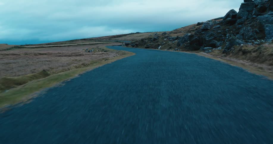 Rural road tarmac with rocks and mountains around on a cloudy day