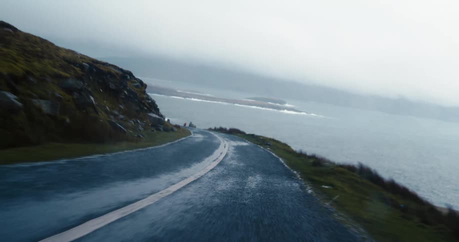 A car driving along a foggy road next to the water