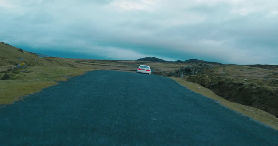 A white sports car drives on a remote road in overcast weather