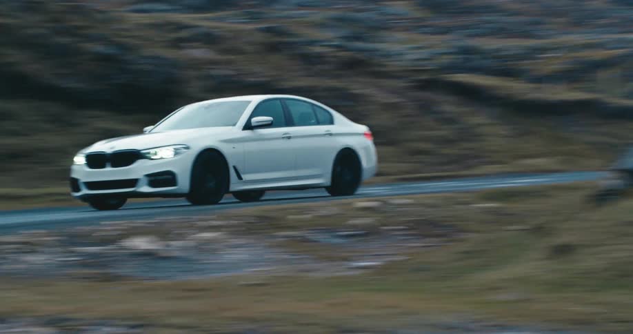 A white car speeding over a paved road in hills