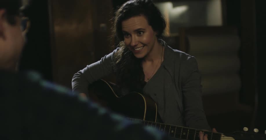 A woman is playing a guitar as a man watches