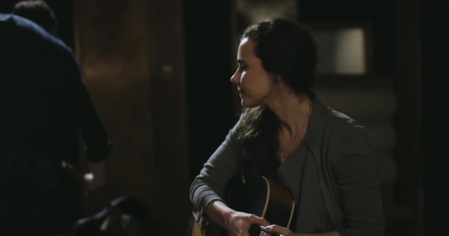 A man talking with a woman stands up and puts away a guitar