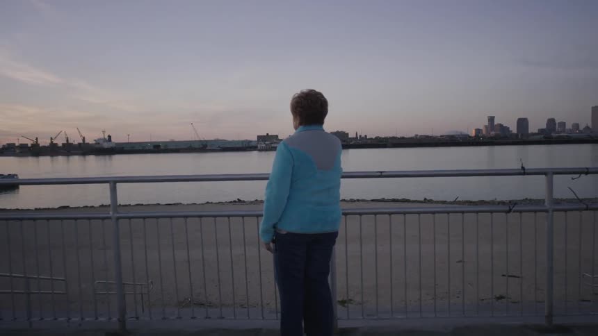 Woman standing at a railing looking out at the waters across from a large city