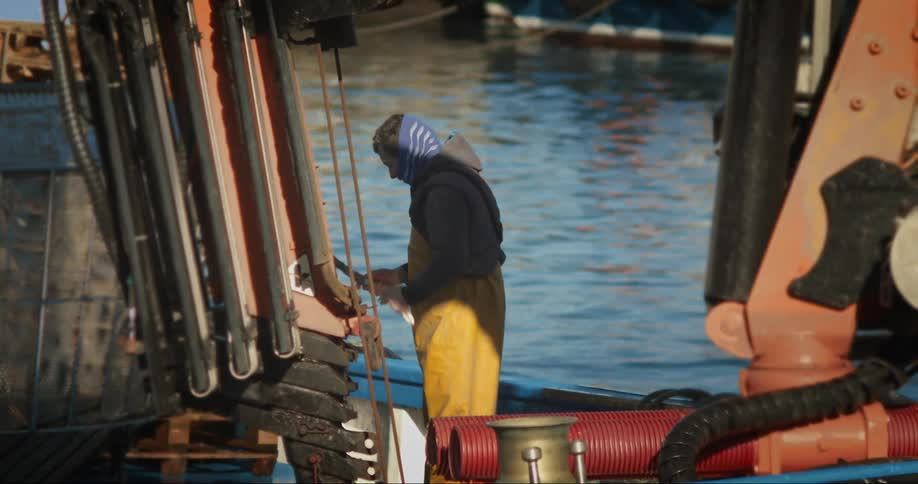 A man on a dock cutting a rope with a knife with water in the background