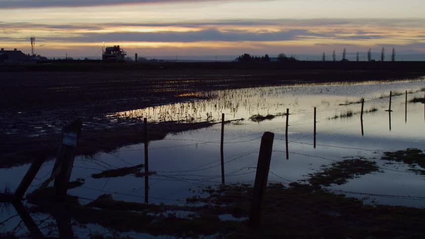 A grassy field with a fence flooded with water with the sky and clouds in the background