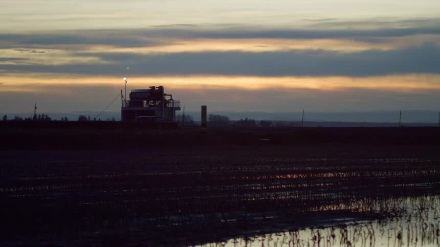 A silhouetted rural structure in a field at sunset