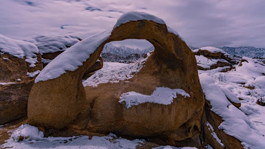 Rocks covered in snow with a mountain range the sky and clouds in the background