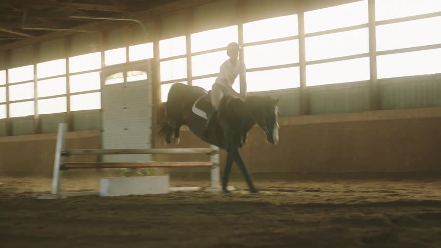 Woman rides a horse over an obstacle indoors