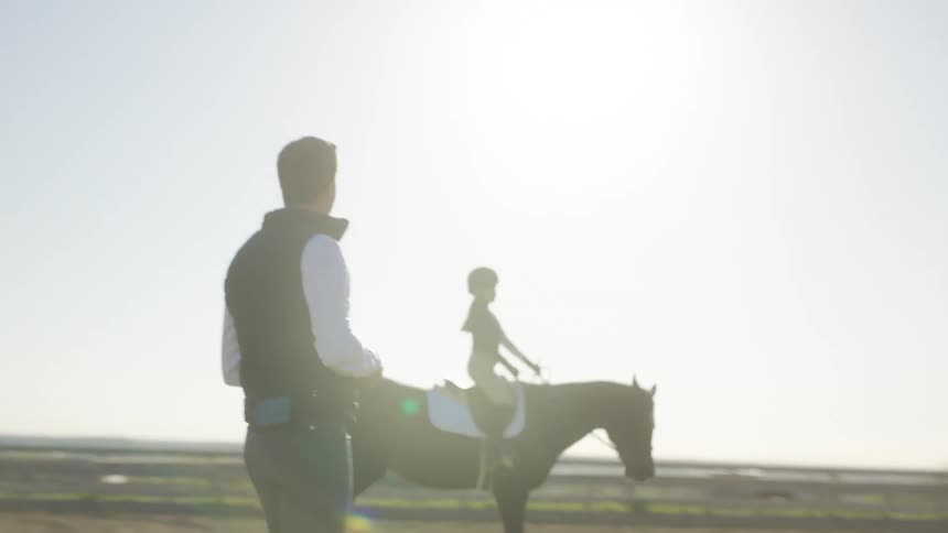 A horse rider instructor teaching a girl how to ride a horse in a circle around him