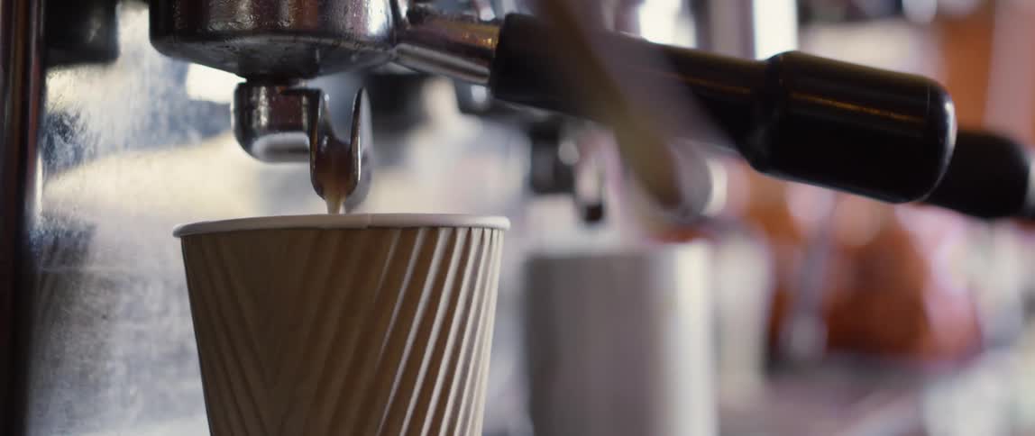 Coffee being poured from an espresso machine into a paper cup