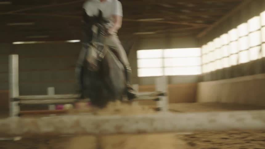 A man on a horse jumping over hurdles with walls and windows in the background