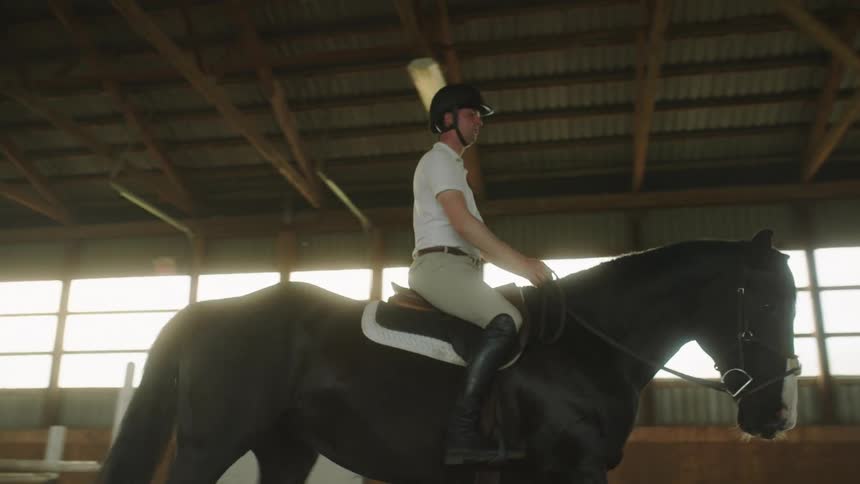 A man rides a rose around an indoor riding arena during the day