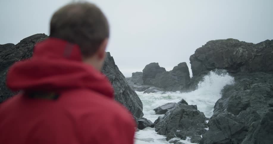 A man is watching the waves crash against the rocks