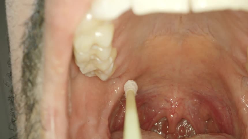 A man in a room taking off a mask and a swab entering into his mouth
