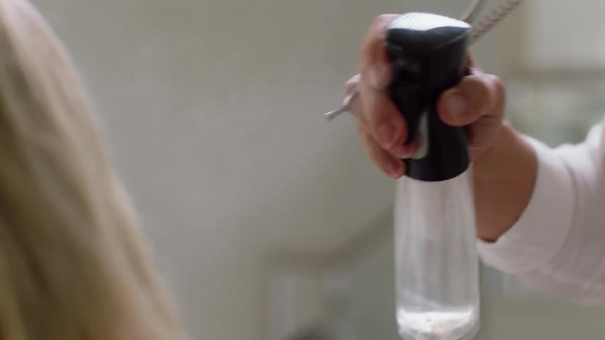 A hair stylist uses a spray bottle to spray the hair of a woman indoors during the day