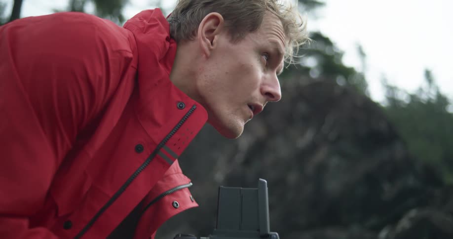 A man outdoors looking down at a film camera and then up to his subject