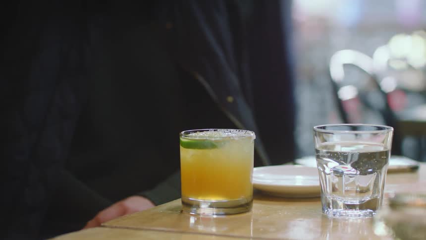 A man sitting in a restaurant with a glass of water and a cocktail in front of him