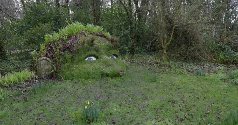 Sculpture of a head peaking out the ground in a forest