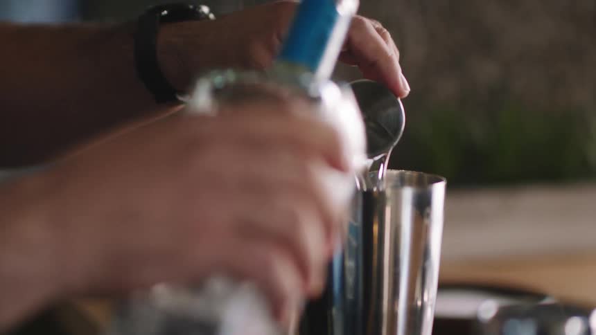 A person pouring vodka into a jigger then into a shaker