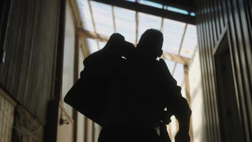A man lifts a saddle off the floor before carrying it down a corridor over his shoulder