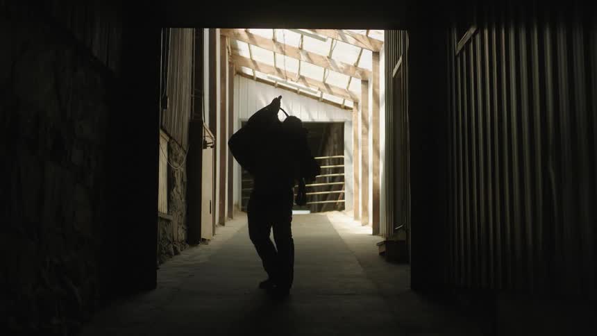 Silhouette of a man picking up a saddle and carrying it across the barn