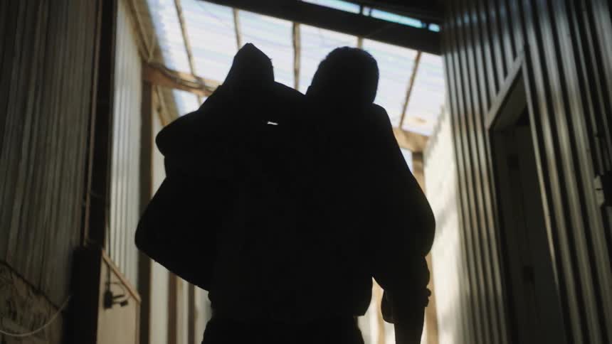 Silhouette of a man in a hallway picking up and carrying a horse sadle over his shoulder