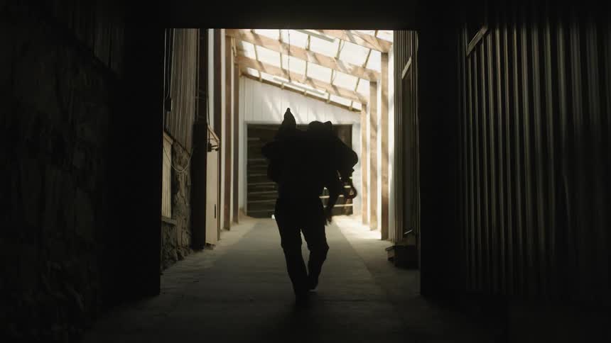 A man picks up a saddle from the barn floor and walks away with it