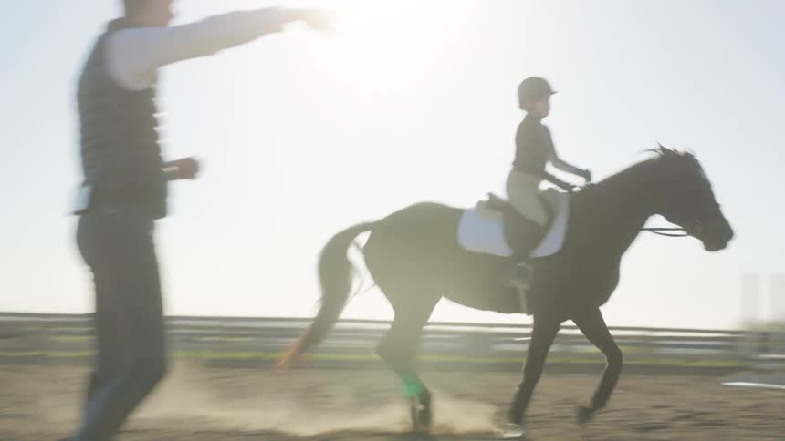 A girl takies equestrianism classes from an instructor in a corral in a rural area