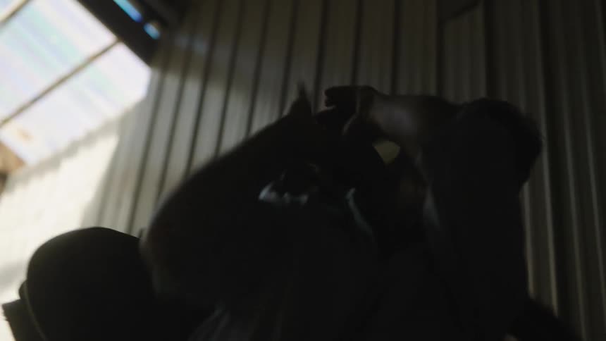 Silhouette of a man picking up a heavy bag swinging it over his shoulders in a dimly lit hallway